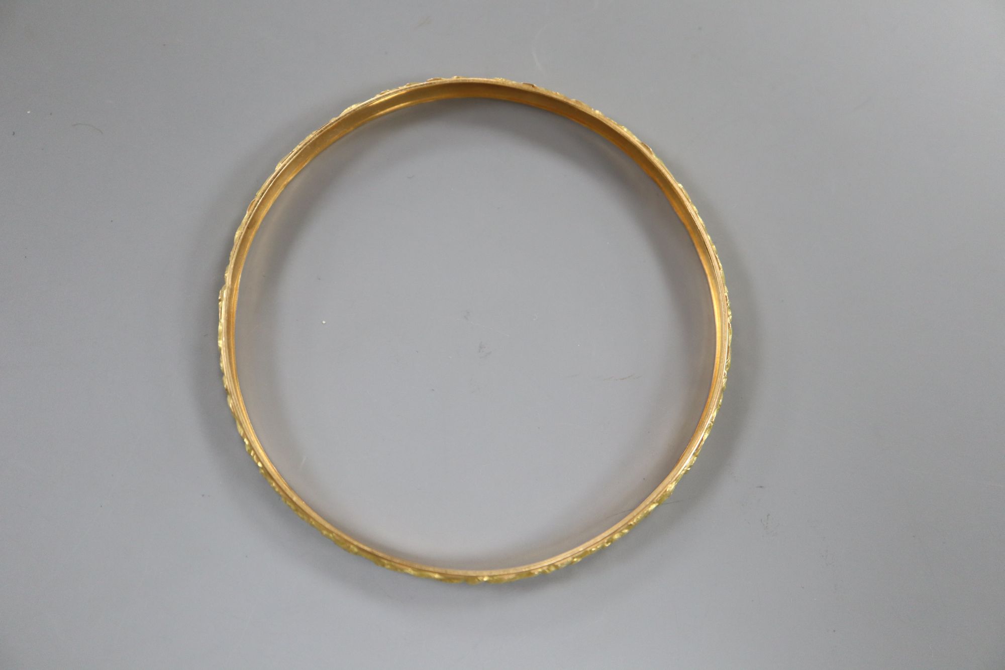 A yellow metal (tests as 18ct) bangle cast with continuous band of flowers, 9g,